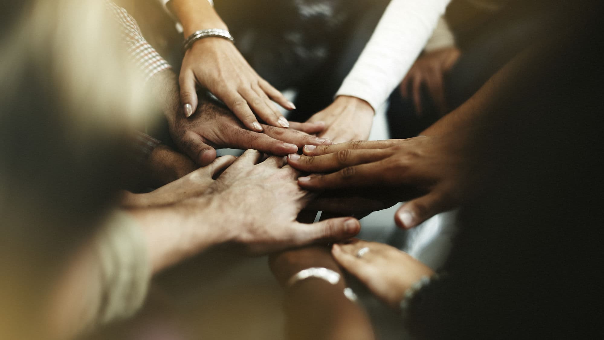 A team stacking their hands together in the middle of a circle, a sign of partnership.