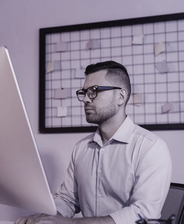 A designer at a desktop computer, a board of notes pinned behind them.