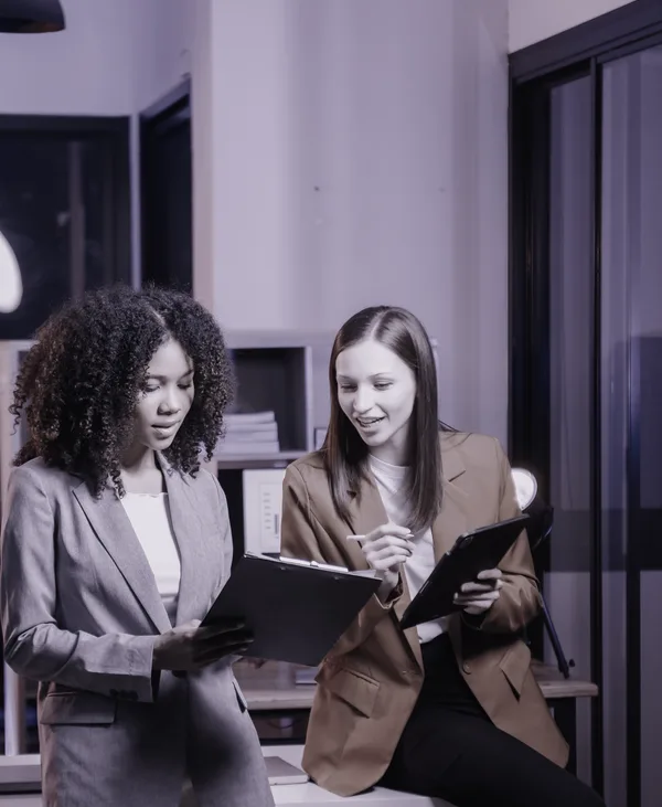 Two colleagues reviewing notes on a clipboard and tablet together.
