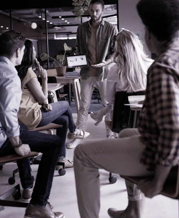 A team presentation, charts shown on a tablet to seated colleagues.