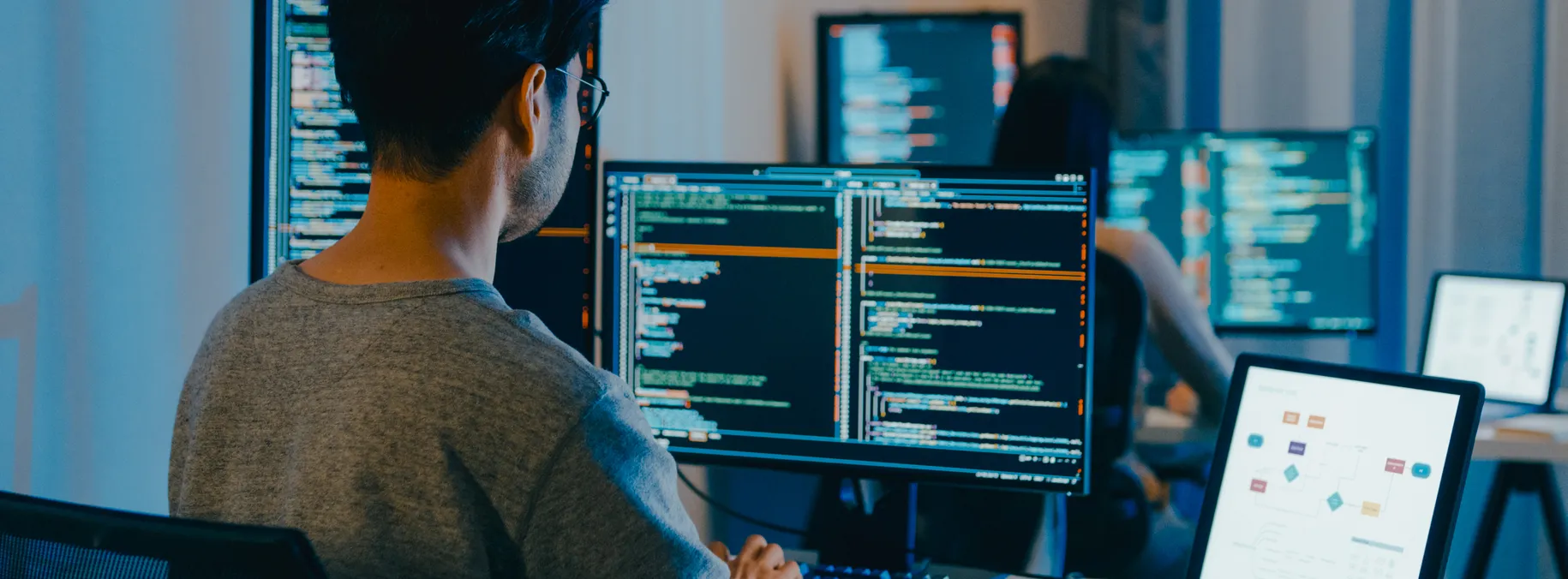 A developer writing code at a multi-monitor workstation.