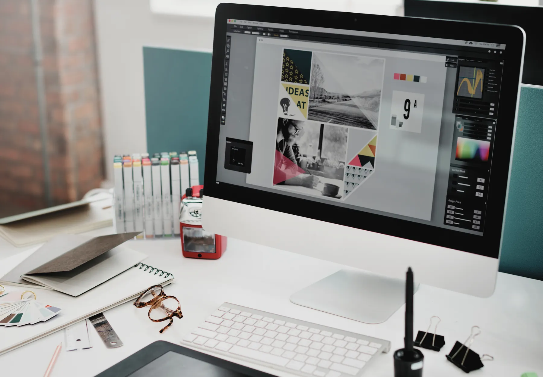 A designer's desk with a moodboard layout on a monitor, markers and colour swatches.